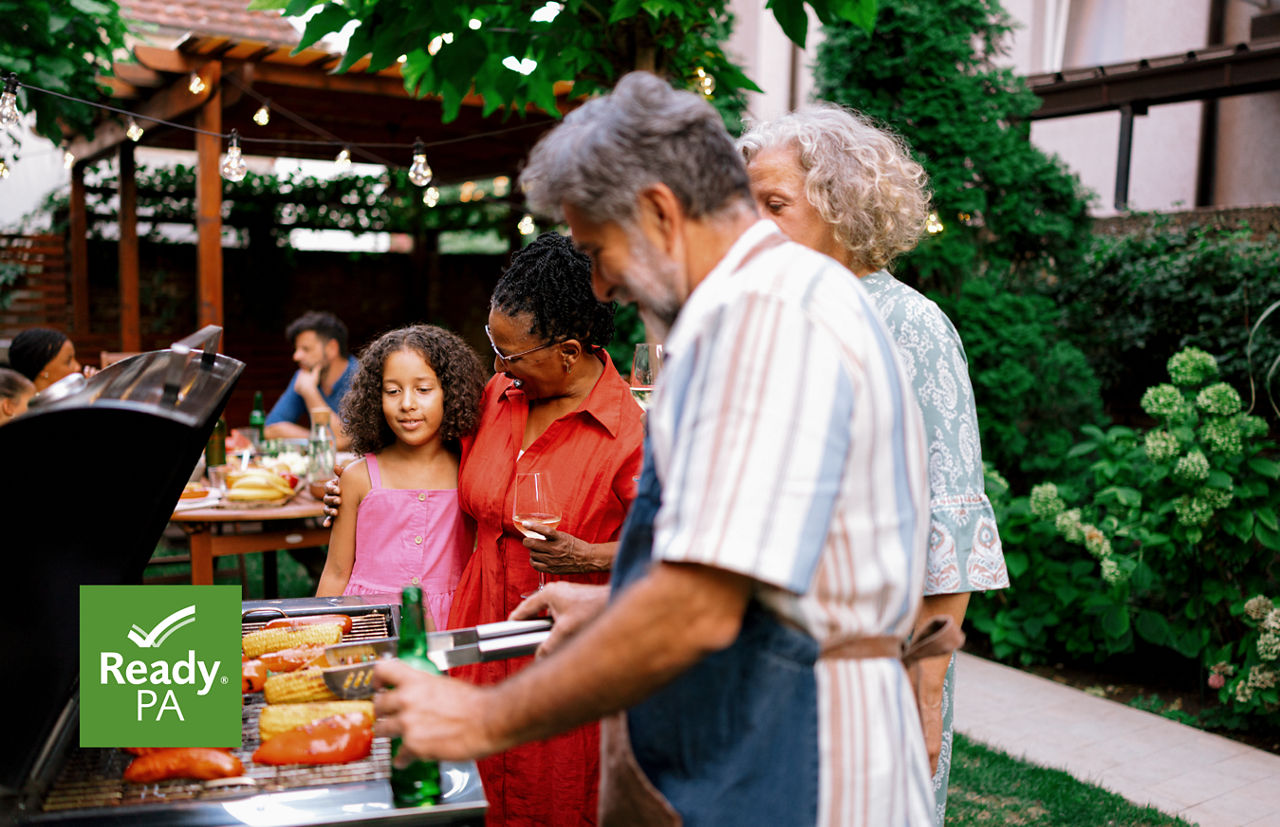 A family grills together in a lush backyard.