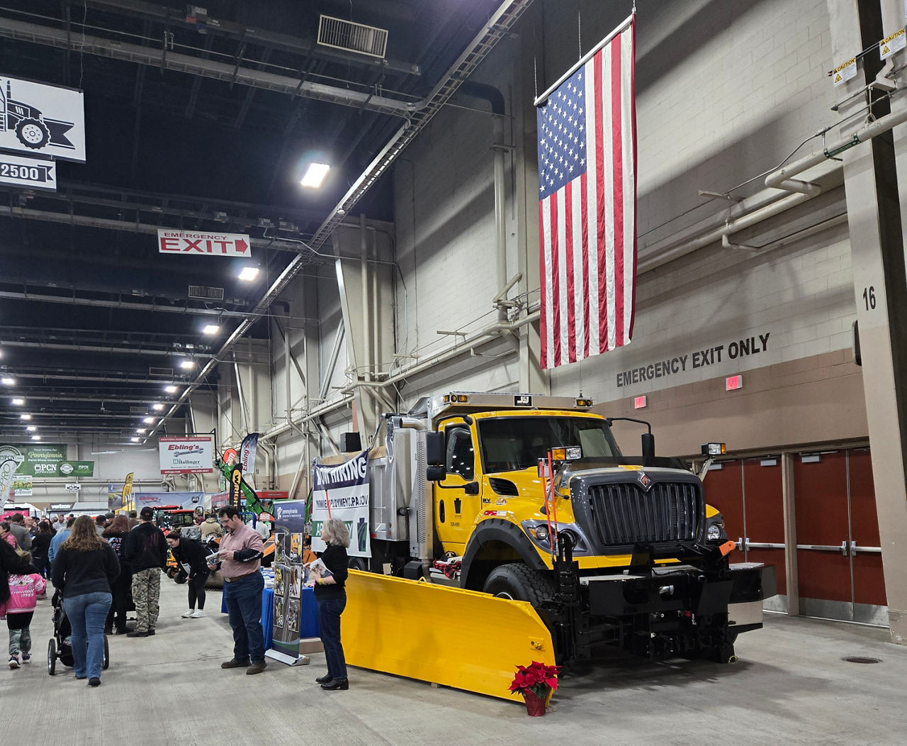 Image of people standing in front of a PennDOT plow truck underneath and United States flag.