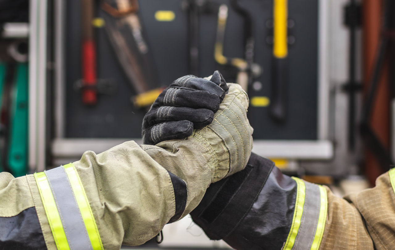 Two people in firefighter gloves and gear shake hands.