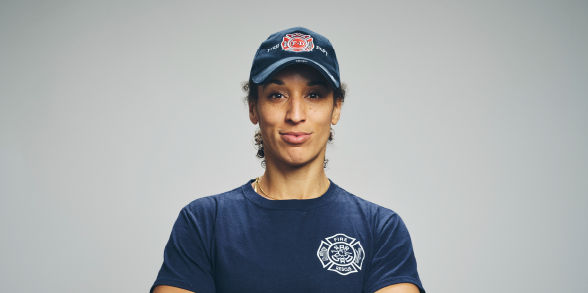 A female firefighter stares into the camera while wearing a blue company hat and T-shirt.