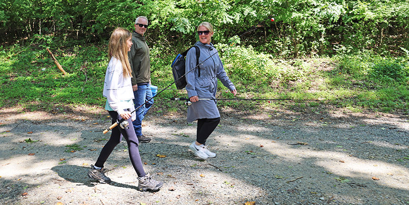 Family of three, a man, woman and young girl, hike along a path with their fishing rods and gear