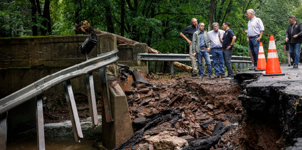 Governor Shapiro and emergency management officials look at flood damage on the side of a torn-up road.