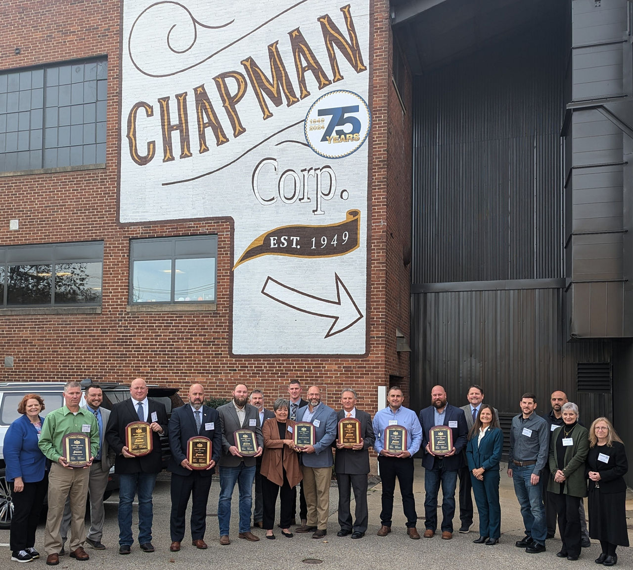 Labor & Industry poses for picture in front of Chapman Corp. building with staff and leadership holding 2024 GASE plaque. 