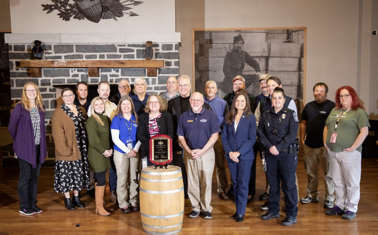 Labor & Industry stands with Gettysburg Foundation leadership holding a 2024 GASE plaque in front of a billboard of a Civil War soldier.