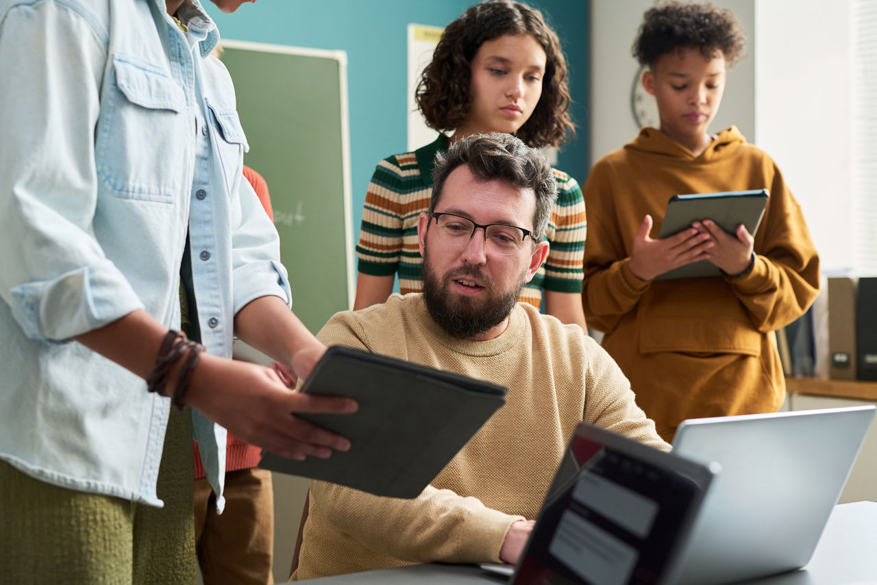 teacher with teen students in classroom all working together on computers and tablets