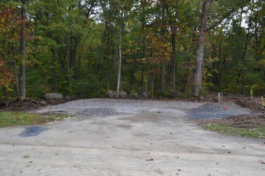 A paved, accessible path meanders through a tranquil forest with bare trees and fallen leaves. A picnic table, designed for easy access, is visible in the background, inviting visitors to enjoy a meal in nature. 