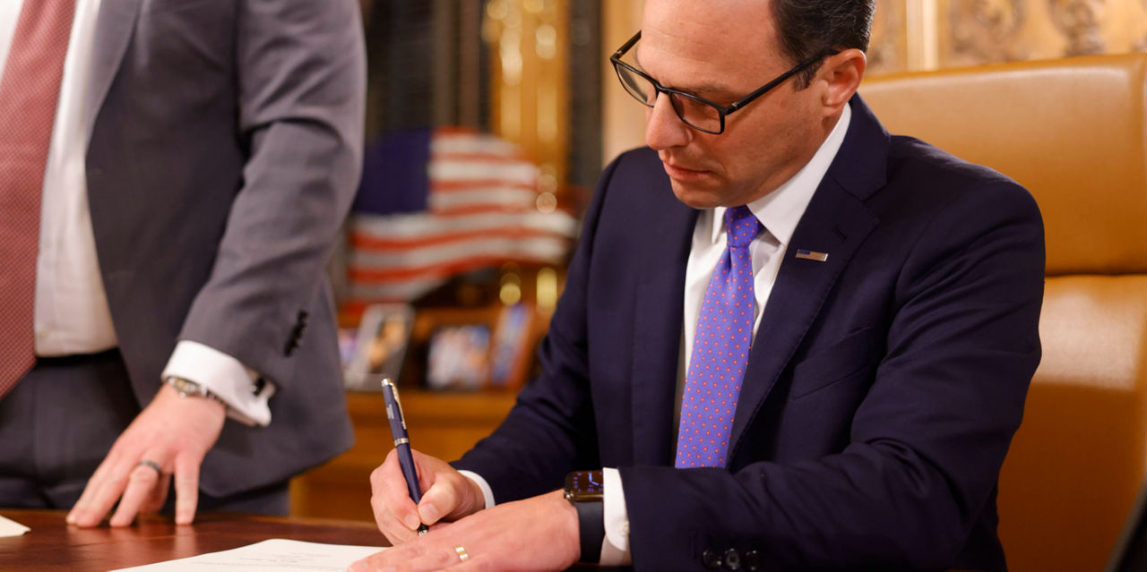 Pennsylvania Governor Josh Shapiro signs a document at his desk.