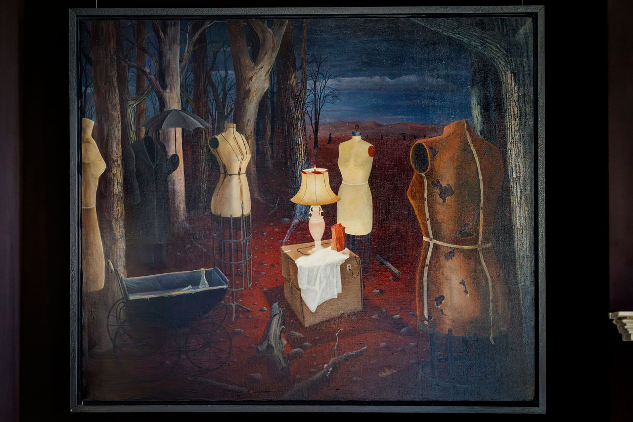 Surreal forest scene with dress forms and lamp.