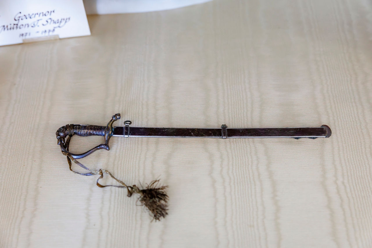 Miniature dress sword with a dark scabbard and braided tassel.