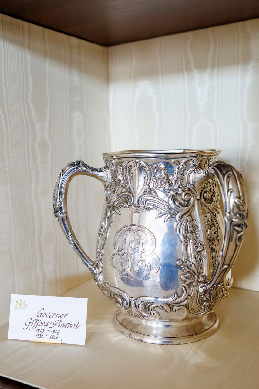 Ornate silver vase with intricate floral designs and initials