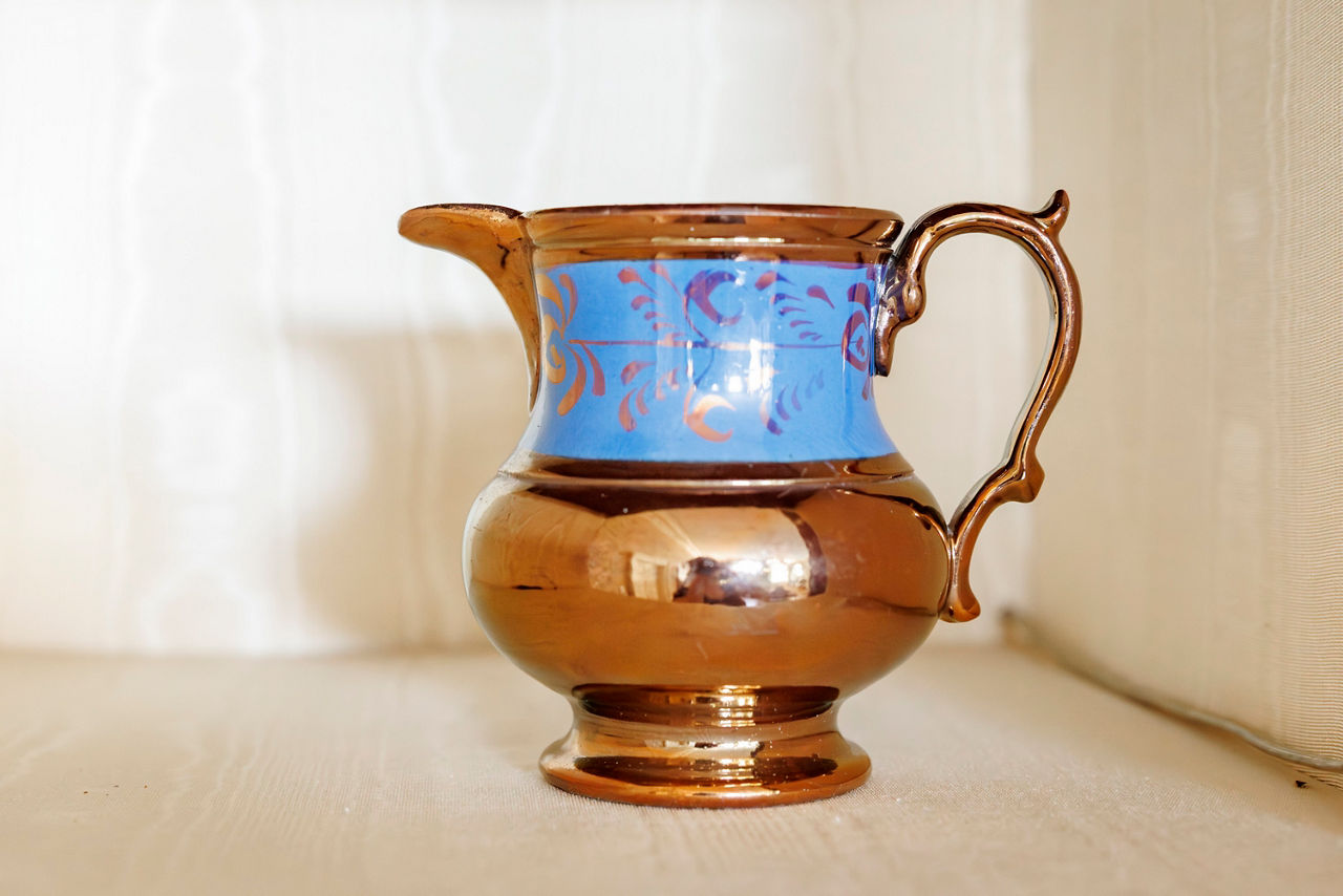Copper luster pitcher with a blue band decorated with swirls.