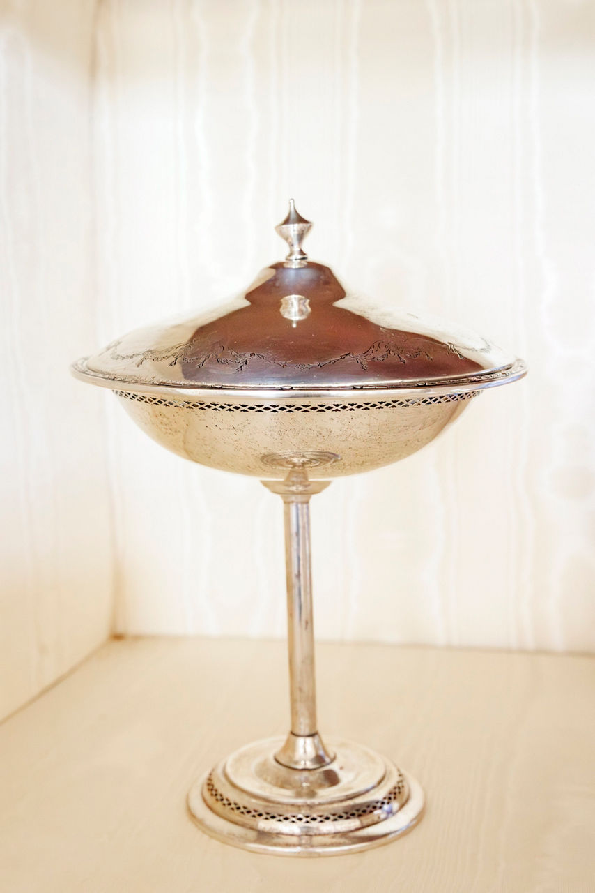 Elegant silver goblet with a lid, featuring intricate detailing, stands on a polished pedestal.