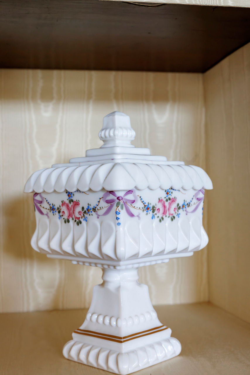 White ceramic pedestal container with lid, adorned with intricate pink rose garlands and purple ribbons