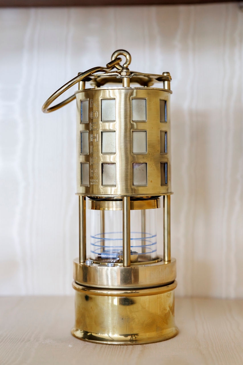 Vintage brass miner's lamp with a cylindrical grill and glass enclosure.
