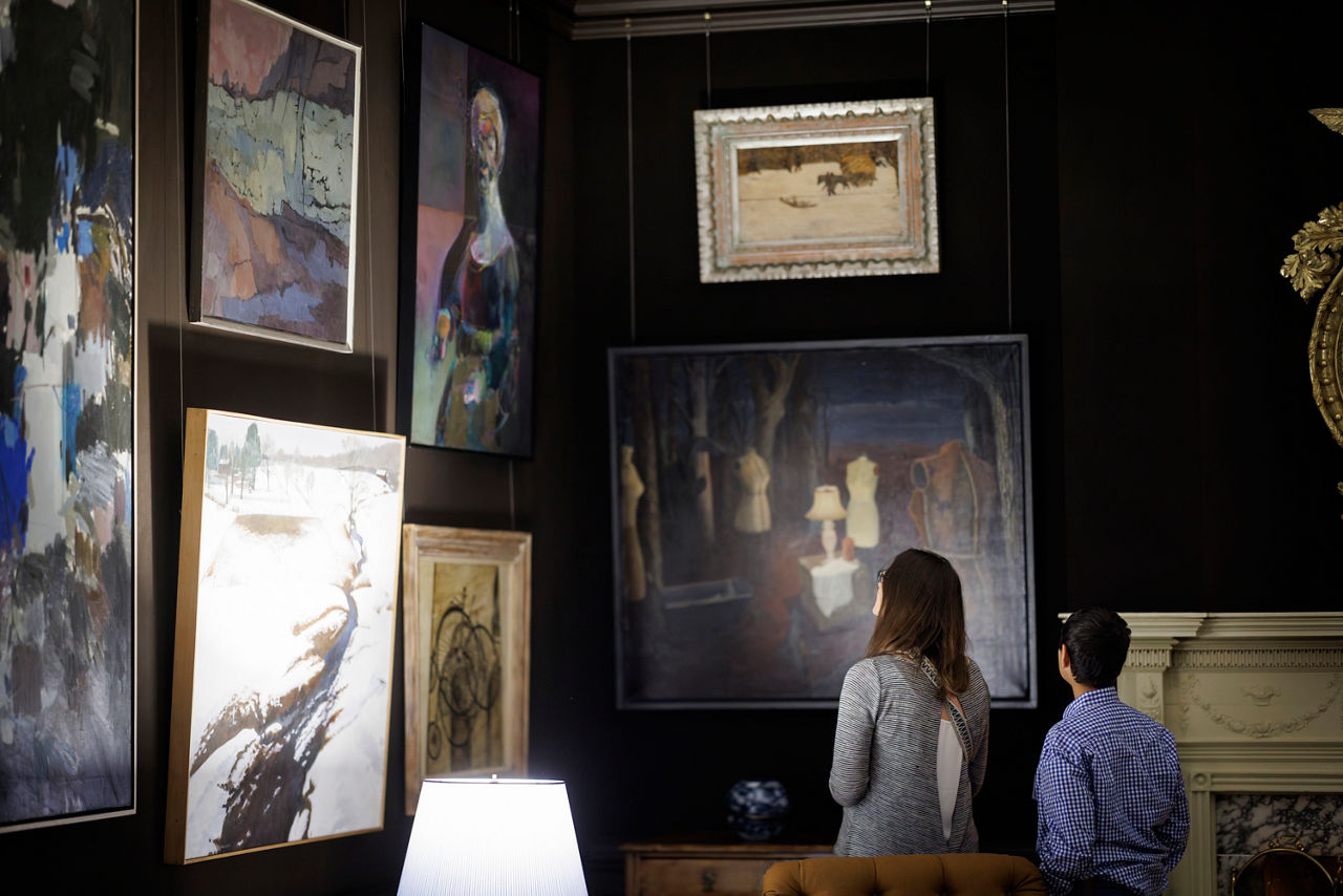 Two people looking at paintings hung on a wall