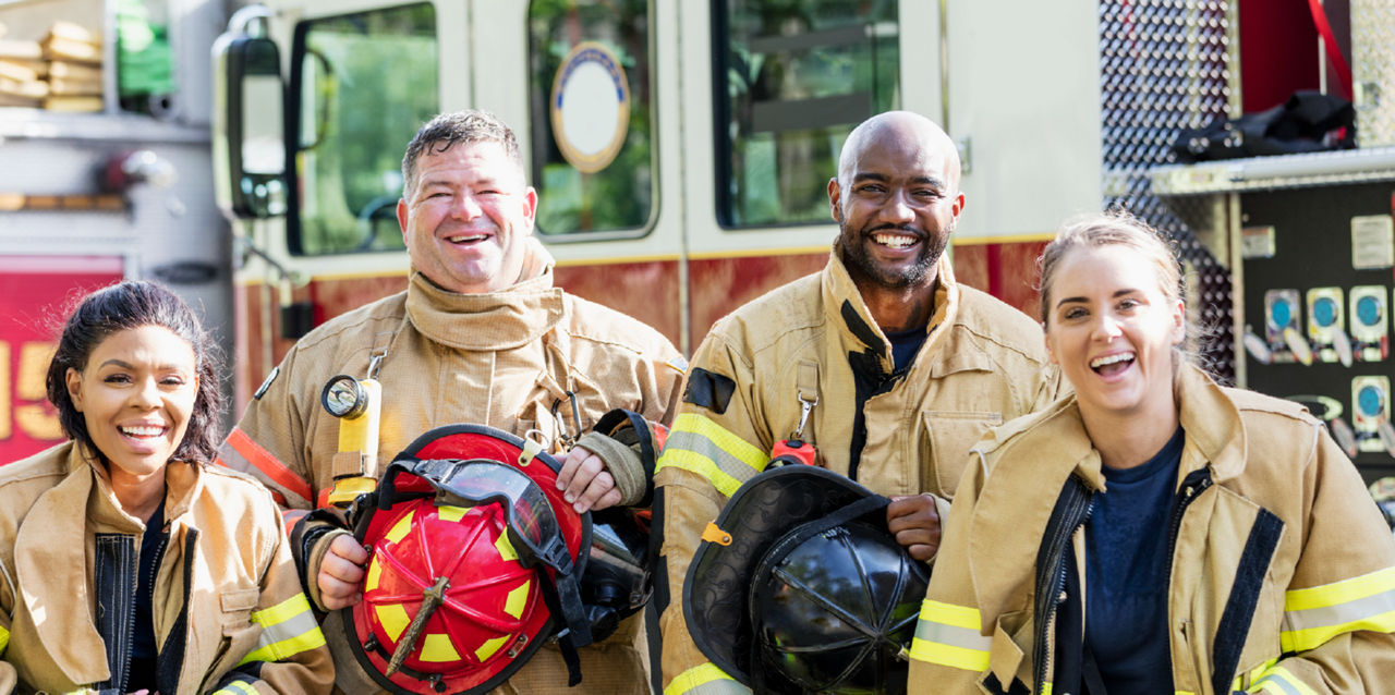 A group of four firefighters in jackets holds their hats and smiles at the camera.