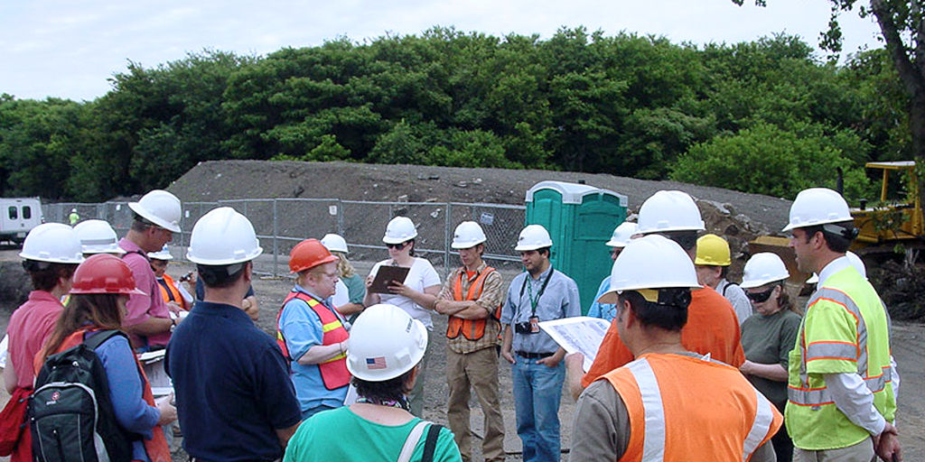 A group of engineers and interested parties wearing hardhats and safety vests discuss cultural resources at a construction location