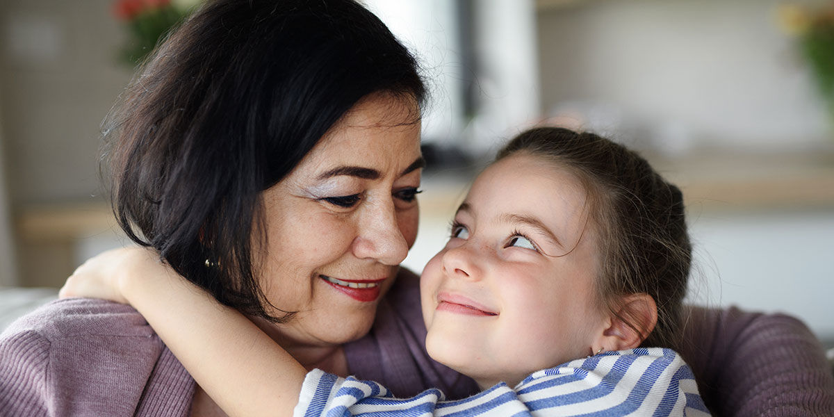 Senior woman hugged by a young girl. They are smiling at each other. 