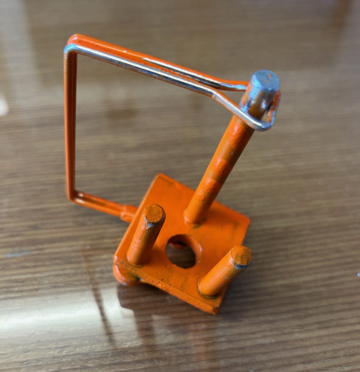 An orange hitch pin with two additional guide pins sits on top of a table.