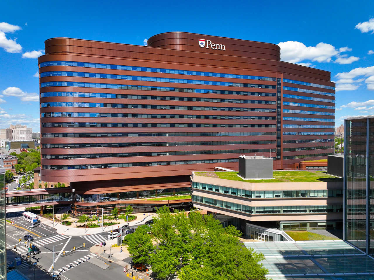 Exterior view of Penn Medicine’s Pavilion in Philadelphia, a modern high-rise hospital building with a curved red-brown facade and large glass windows, with the Penn logo prominently displayed at the top.