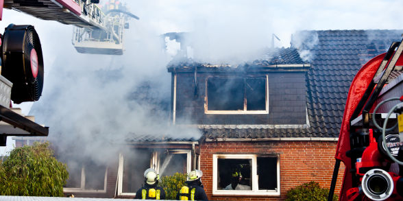 Firefighters battle a fire that is blazing through a red brick home.