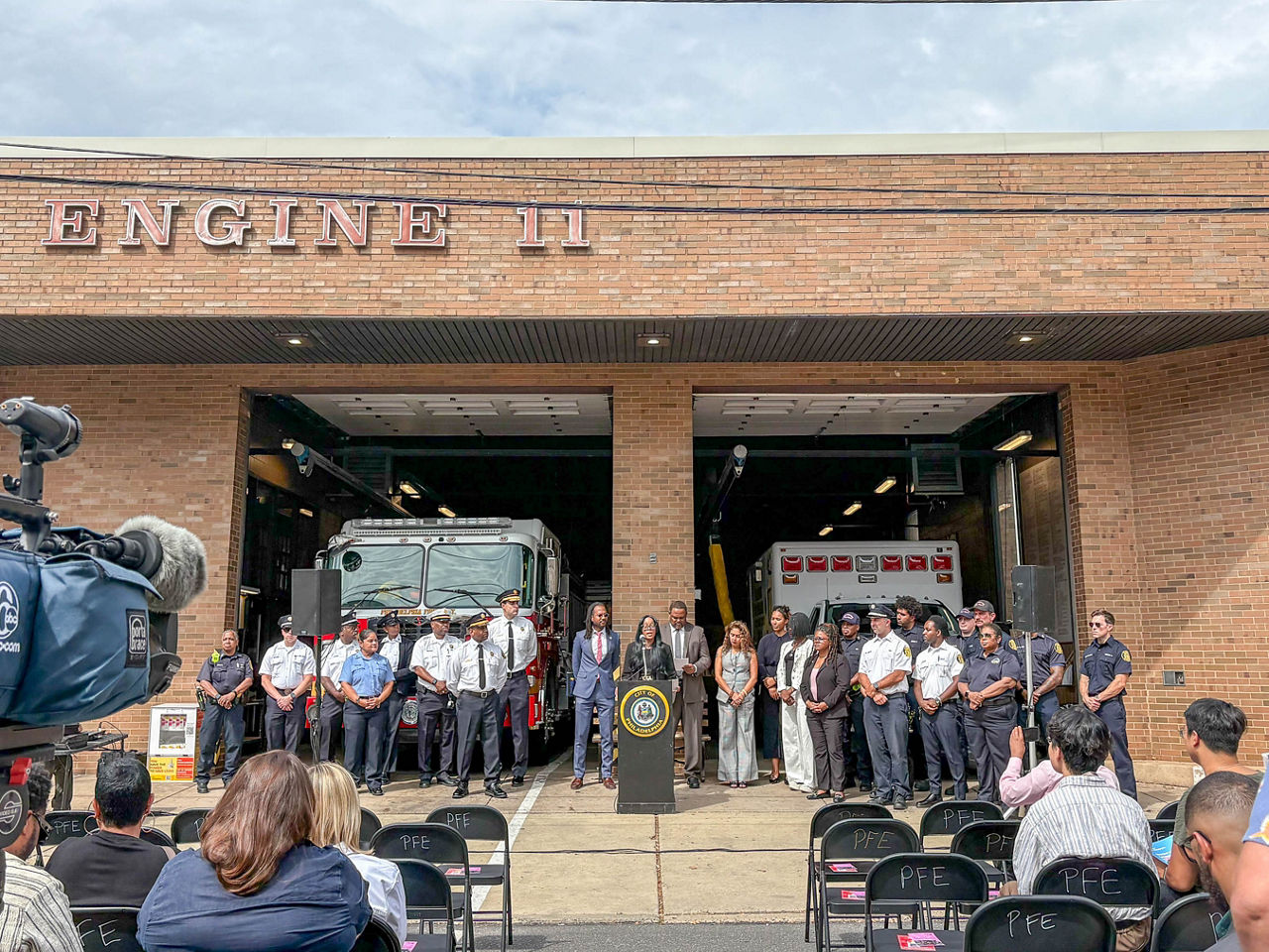 Secretary Dr. Latika Davis-Jones speaks at a podium outside a Philadelphia fire station, with Philadelphia officials and community partners lined up behind her during an Overdose Awareness Day event.