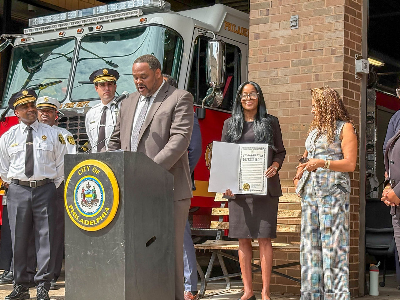 Secretary Dr. Latika Davis-Jones holds Pennsylvania’s Overdose Awareness Day proclamation while a Philadelphia official speaks at the podium outside a city fire station.