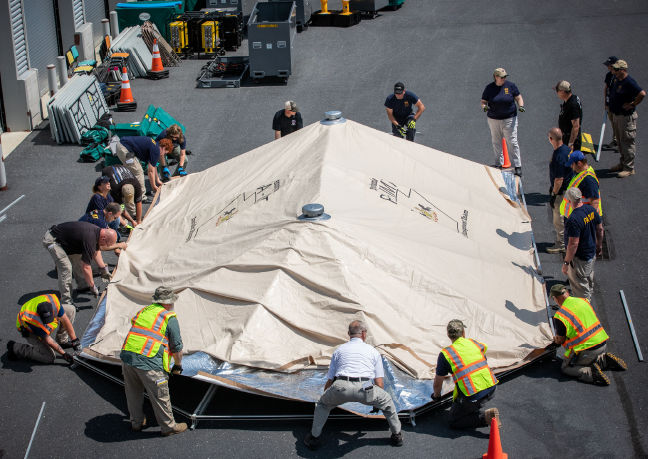 Members of the Incident Management Team stand in a circle while laying out a tarp during an exercise.