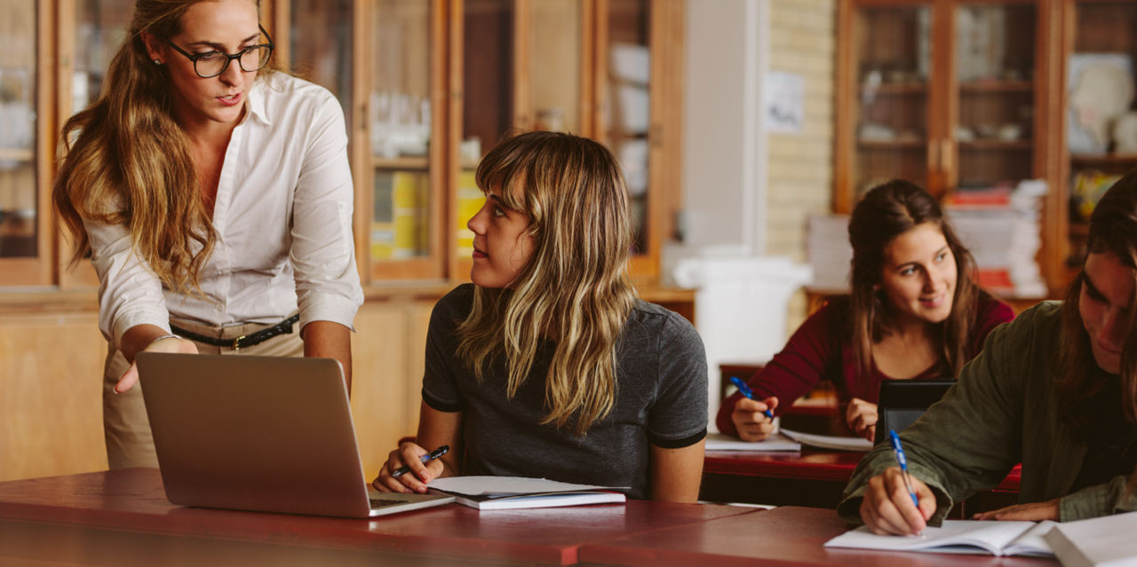 An instructor stops at a student's desk to help with something.