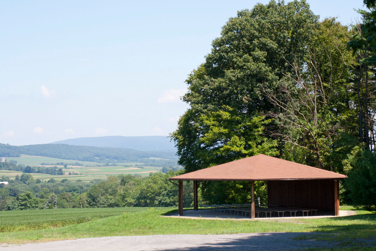 A wooden pavilion surrounded by large trees and a landscape view of mountains and valleys