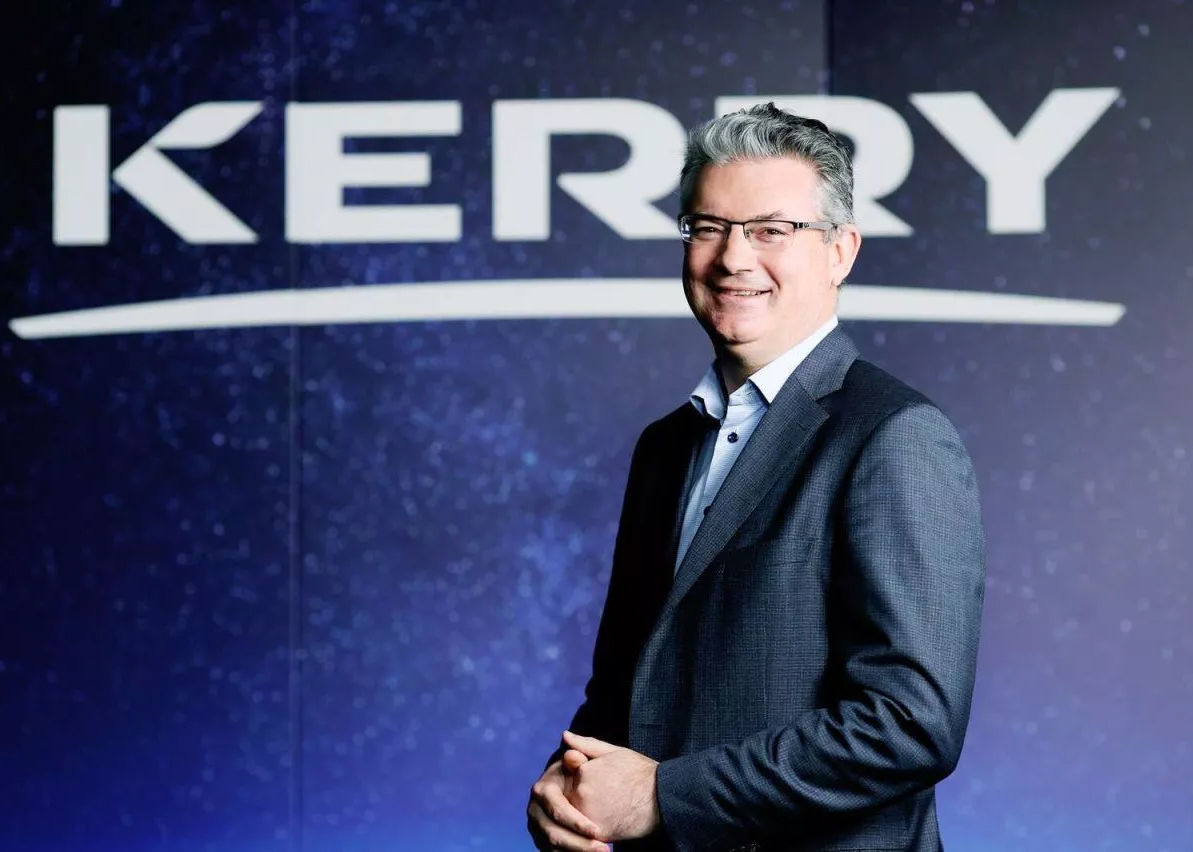 The CEO of Kerry Group poses for a photo in front of the company logo.