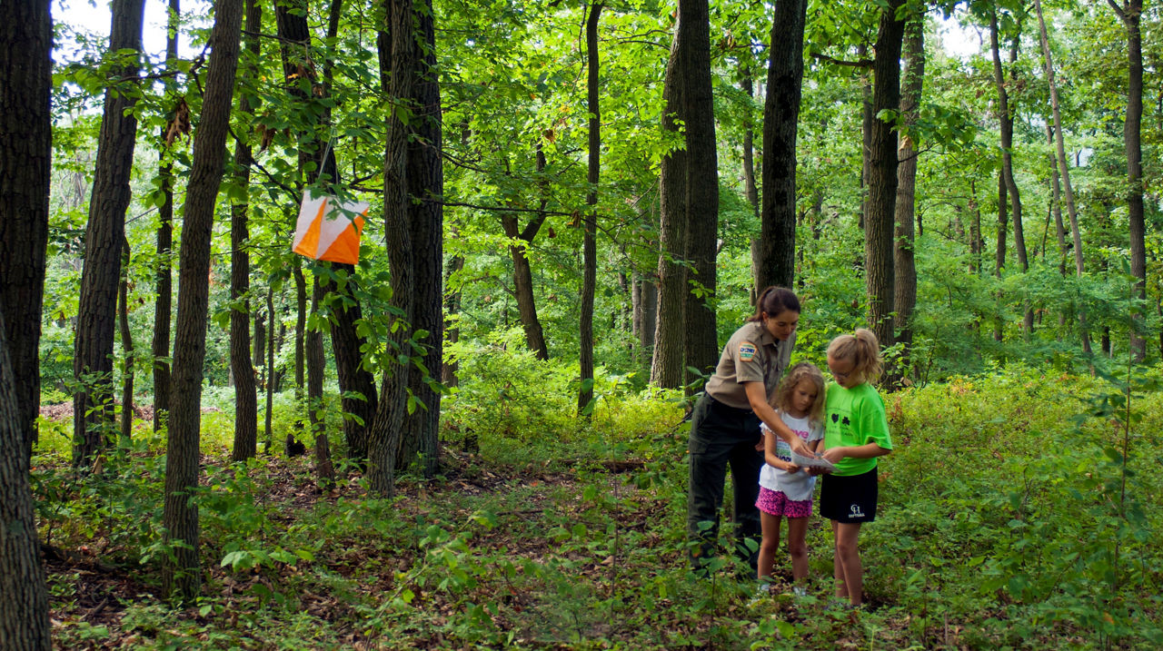 A park educator helps two girls with a map near a temporary orienteering marker