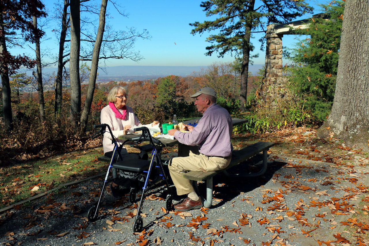 An older couple sitting a picnic table with a valley view behind them