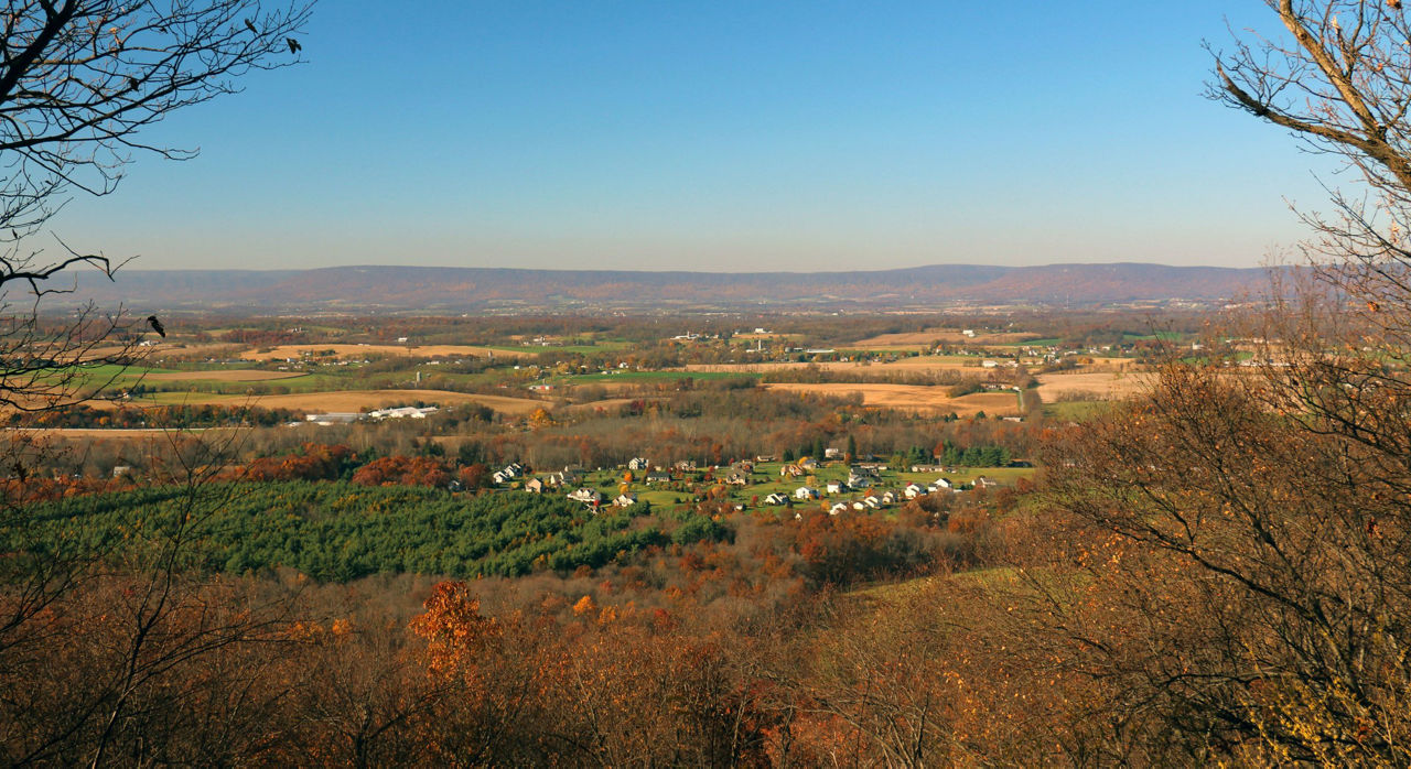 Fall scenic view overlooking a valley with houses, farmland, and forests.