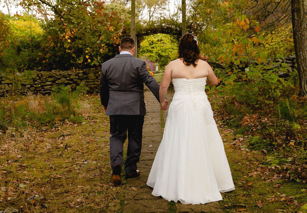 A bride in groom dressed in wedding attire walking on a path covered in golden fallen leaves