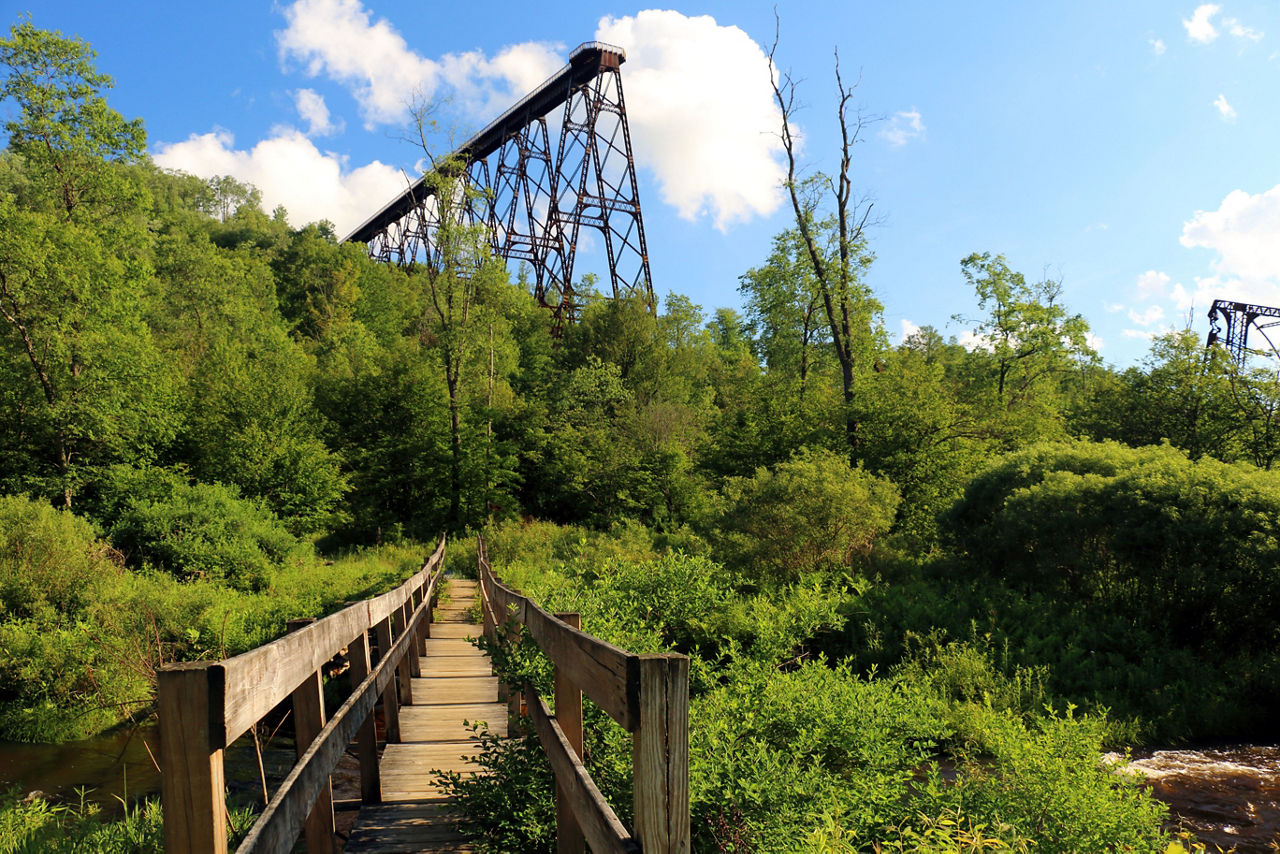 A trail crosses a wooden foot bridge leading toward the skywalk on a sunny day