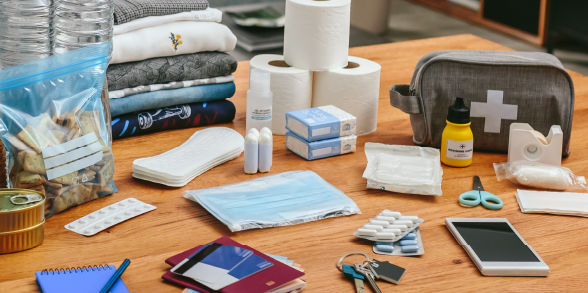 Items on a table, including: medicine, spare keys, documents, a first-aid kit, spare phone, extra clothes, snacks, and hygeine products.