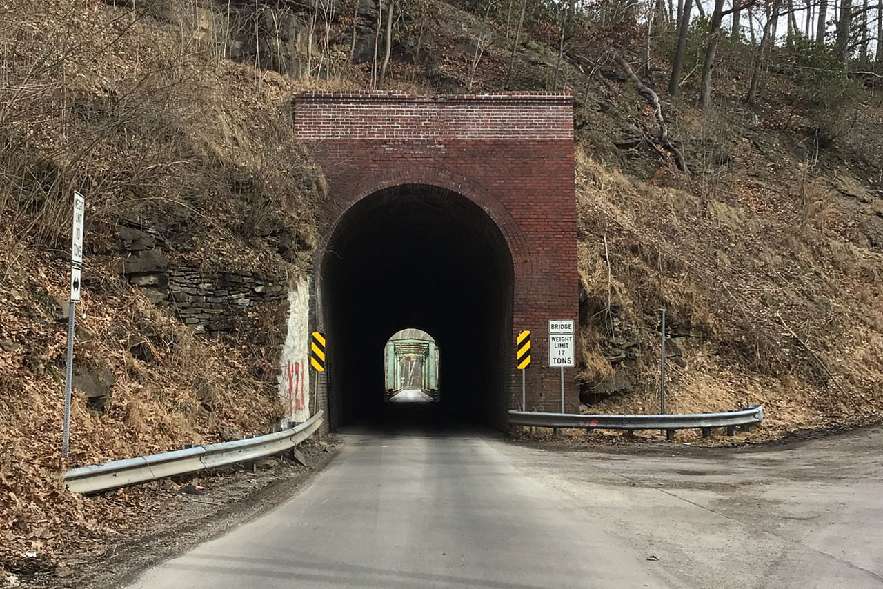 Image of Layton Tunnel, from the roadway you can see the tunnel passing through the slope of a hillside. The road is straight and you can see the other side of the tunnel exit in the distance.