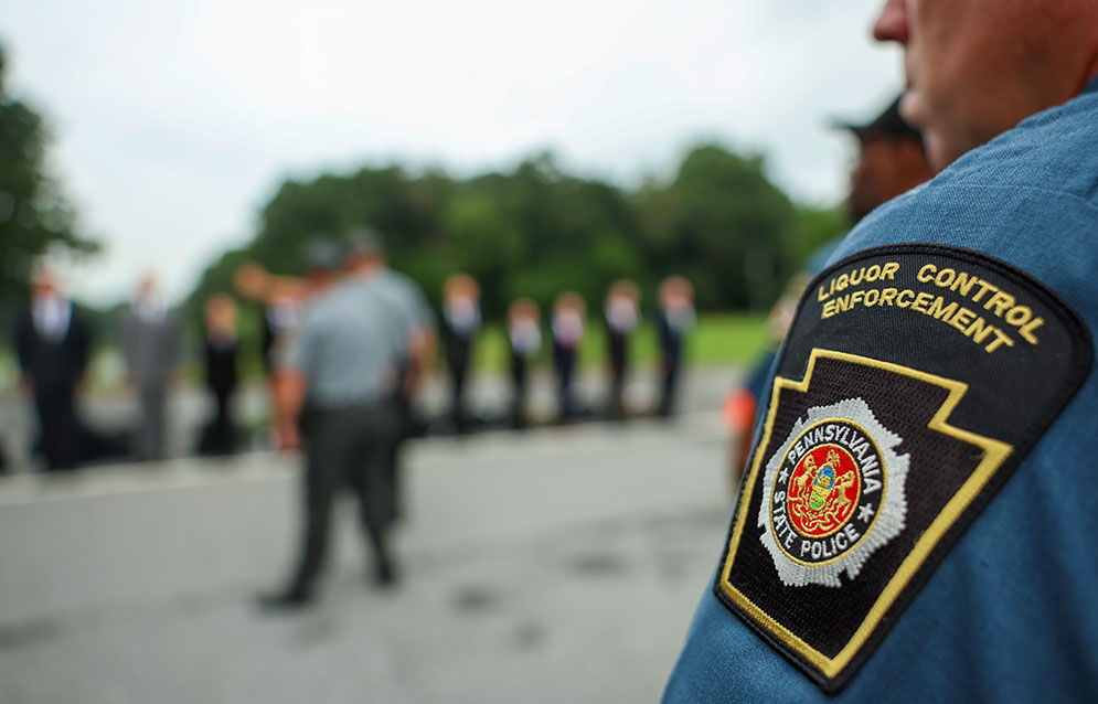 A Liquor Control Enforcement Officer in the foreground watches new recruits in the background arrive for training. His LCE patch is point of focus.