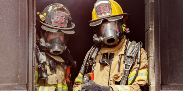 Two firefighters look out of a window.