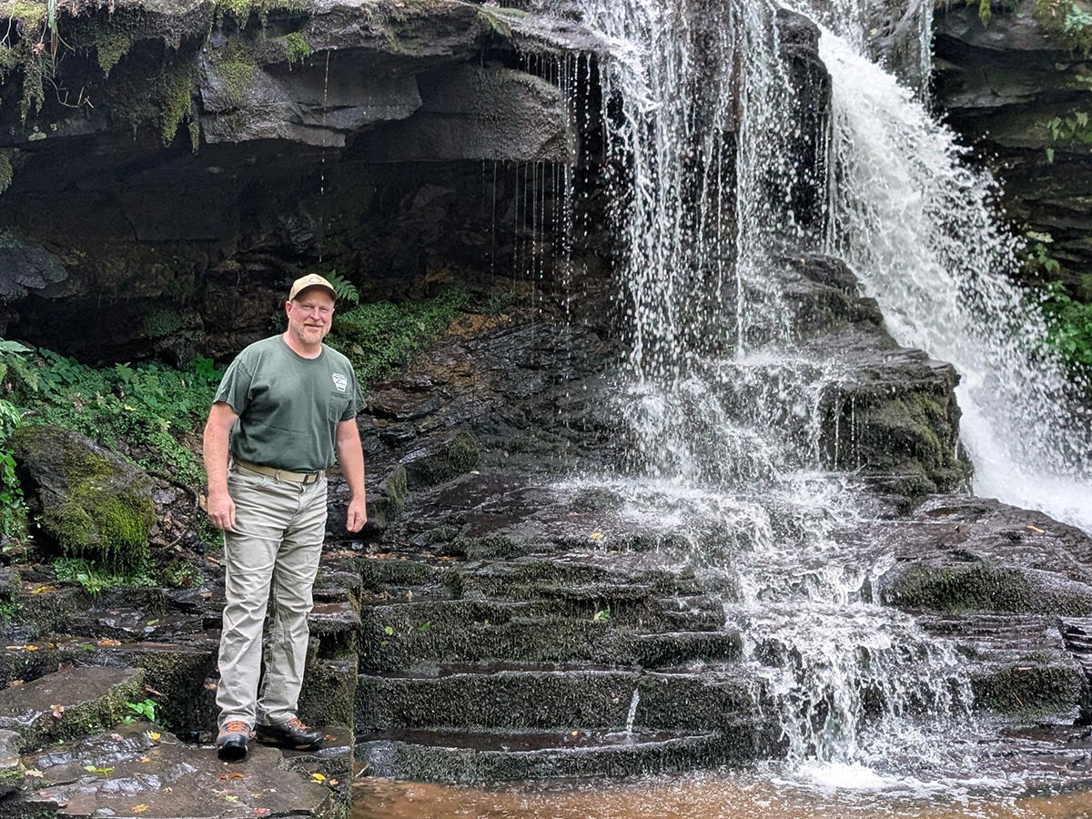 Loyalsock State Forest District Forester Eric Probert stands next to a waterfall.