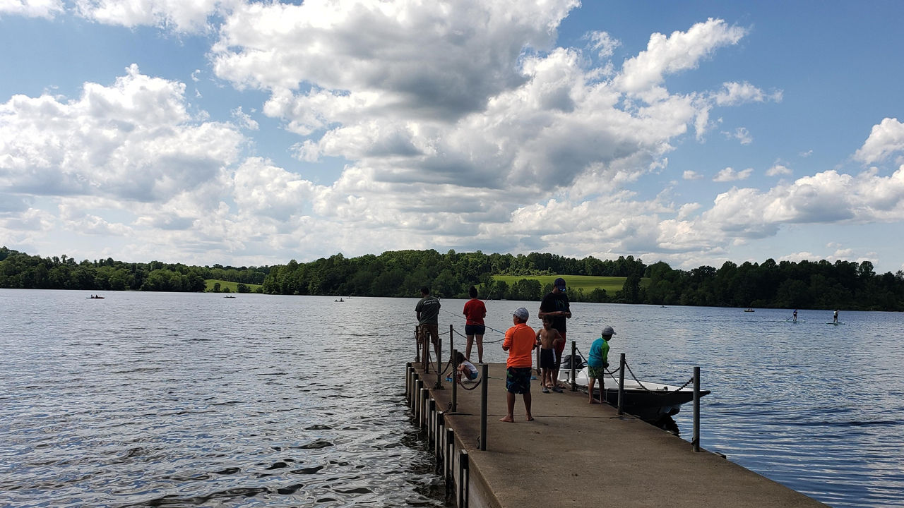 A family fishing on a lake with blue sky and white puffy clouds above