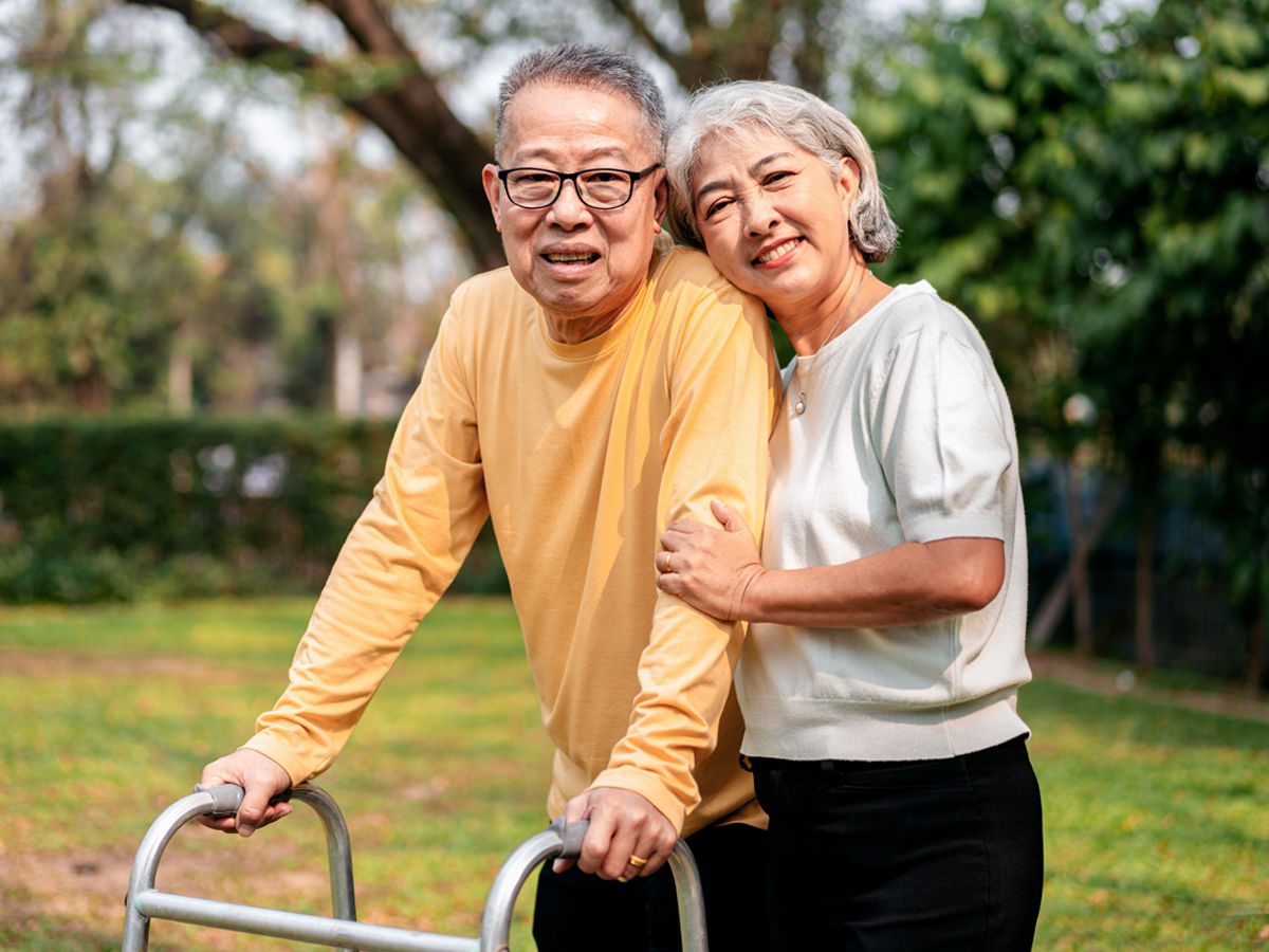 man with walker with woman holding his arm with affection