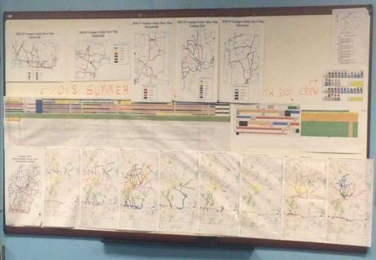 Large Gantt charts and other paper documents are displayed on a white board. 