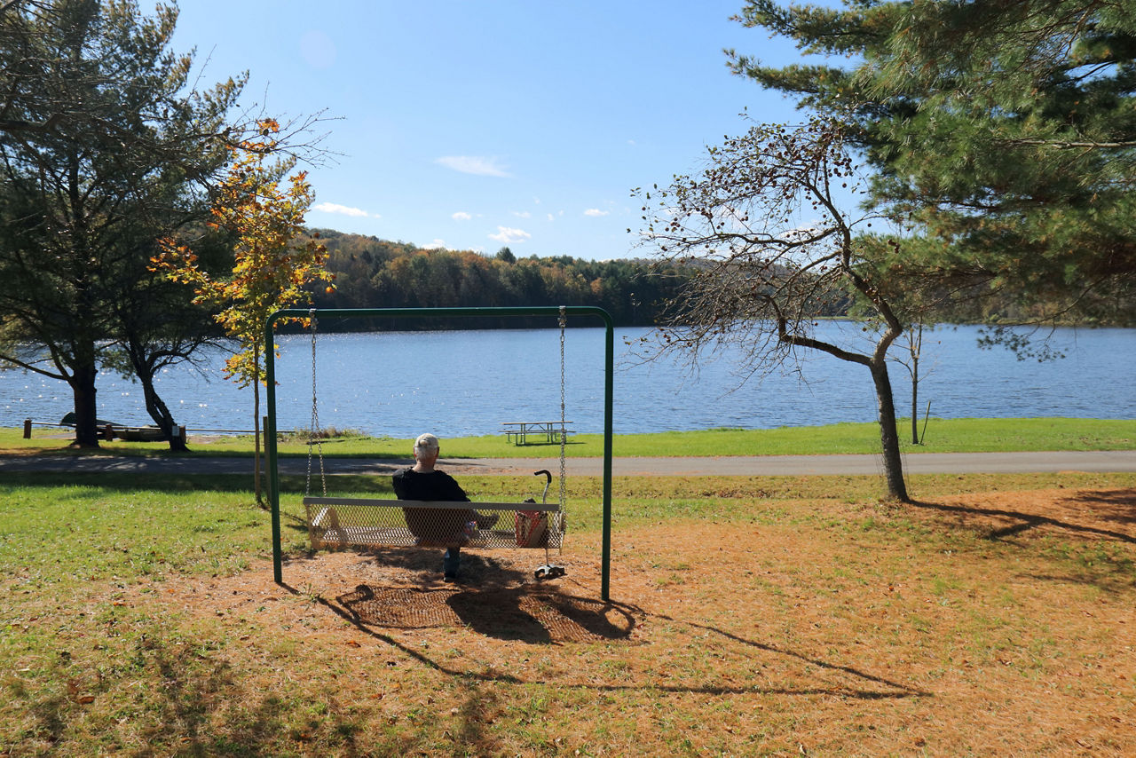 A person relaxing on a bench swing facing the blue waters of the lake