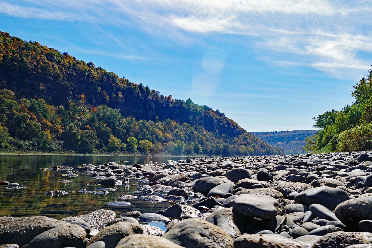 Close-up of the rocks and boulders along the shoreline of the North Branch Susquehanna River with fall foliage mountains in the background.
