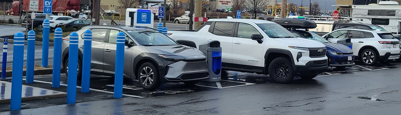 Image of several electric vehicles in designated electric vehicle charging parking spots. 