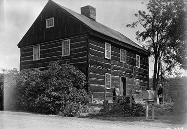 One story log house with a steep roof and hillside setting.