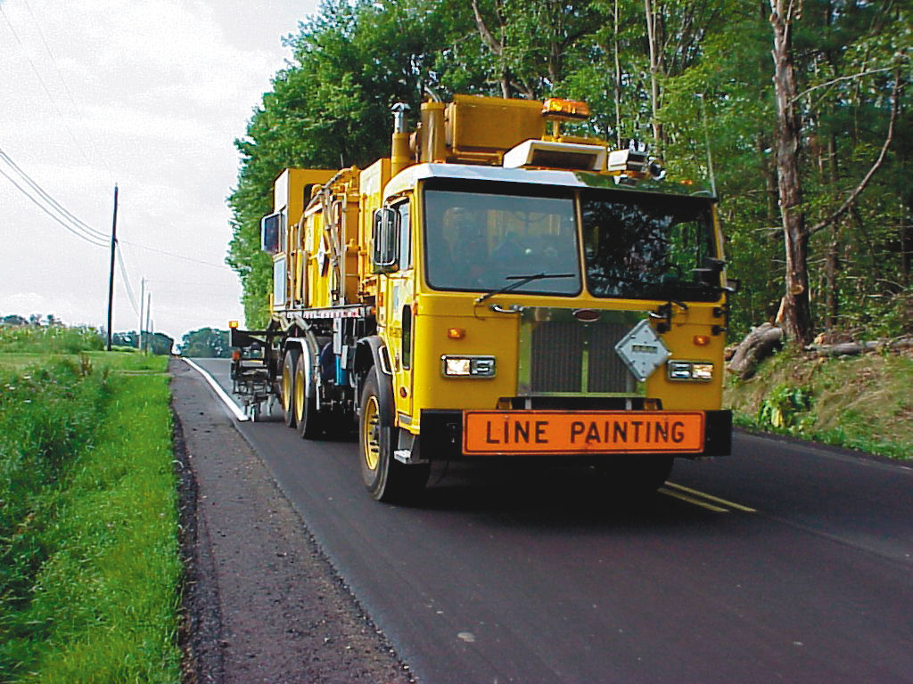 A yellow line painting truck painting white lines along the side of a roadway.