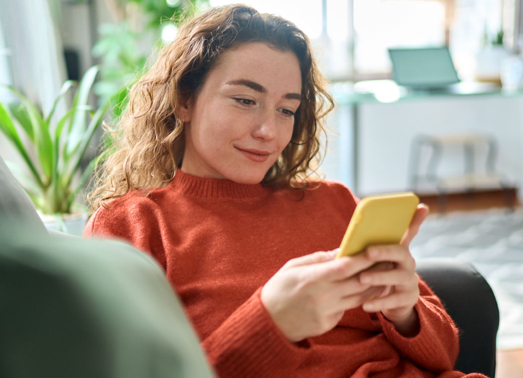 A young woman checks her phone from the comfort of her couch.